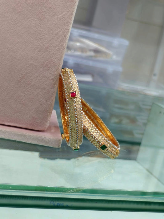 Luxurious gold bangles with ruby, emerald, and pearl details.